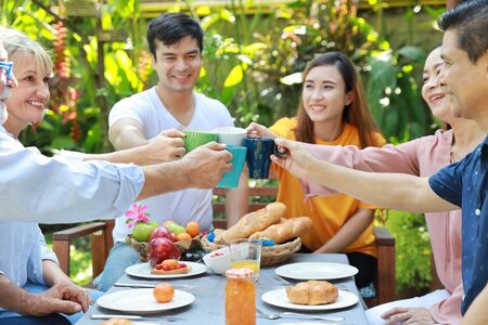 Happy multiethnic family sitting at a breakfast table in backyard outdoor on sunny day with smiling face while everyone clicking glasses.の写真素材