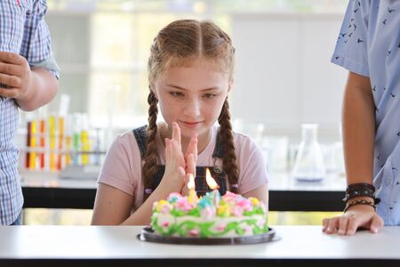 cute little caucasian girl blowing out candles on homemade baked cake with friends (celebrating or birthday concept)の写真素材