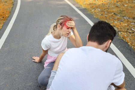 young girl fall down because of the dizziness from too much exercise and young man is helping in the parkの写真素材