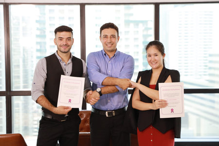 two caucasian businessmen and asian businesswoman shaking hands while holding success business...