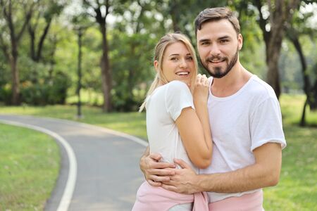 young caucasian couple are in love. man and girl wearing white shirt hugging in the park during summer season with smiling and happy faceの写真素材