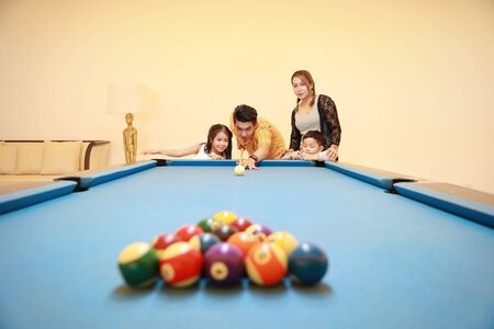 group of happiness asian family father, mother, son and daughter playing billiard or snooker on blue pool table with happy smiling face during holiday vacationの写真素材