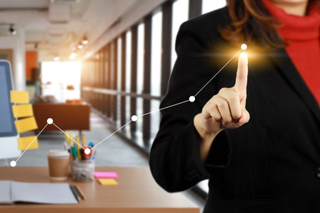 Businesswoman in black suit drawing graphics a growing success business graph with modern office blurred background using for business growth concept backgroundの写真素材