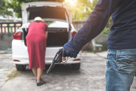 thief with gun trying to steal car or money from unaware woman with automobile (theft concept)の写真素材