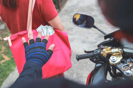 thief on motorcycle with gun trying to steal bag or money from unaware woman on street (theft concept)の写真素材
