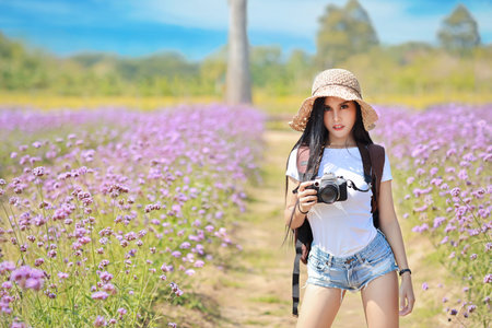 Asian beautiful woman, long hair in white shirt with camera and hat on Verbena filed with blue sky....