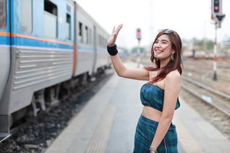 portrait of young asian woman in green dress with sun glassess raising hand to someone in train...