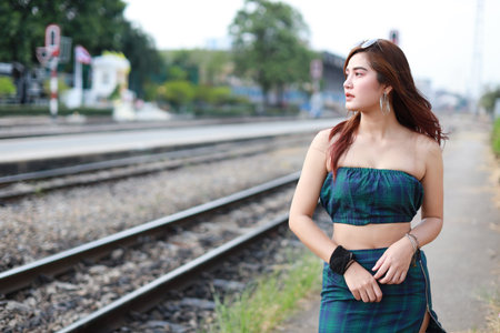 portrait of young asian woman in green dress with sun glassess looking away in train station with...