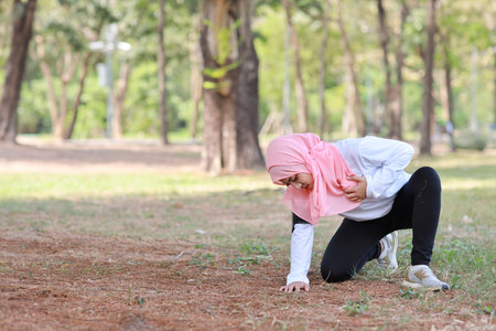 Beautiful young asian muslim girl in sportswear keeps both hands on chest or breast and pain after...
