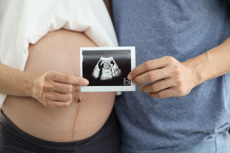 close up shot of young pregnant belly wife and husband hands holding ultrasound film