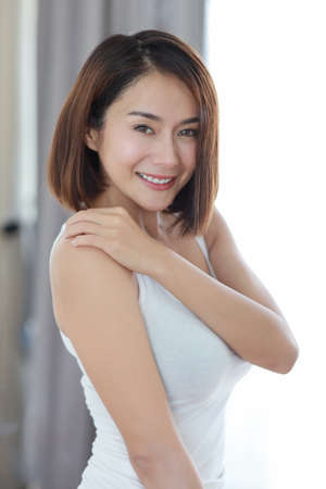 half length young adult asian woman, short hair in white dress with beauty face and looking camera with window lightの写真素材