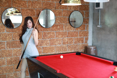 beautiful and sexy asian woman in grey dress playing billiard or snooker on red pool table with...