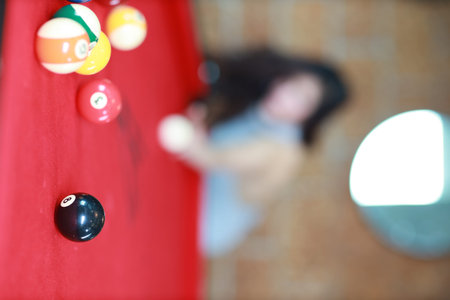full length young beautiful asian woman playing billiards ball on red pool table in club (focus on...