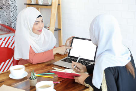 new generation businesswoman muslim people meeting in coffee shop with computer and coffee cup on wood deskの写真素材