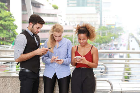 half length shot of happy smiling caucasian young businessman and businesswoman in formal wear, they arguing and discussing startup project with smart phone while walking during lunch break with urban view backgroundの写真素材
