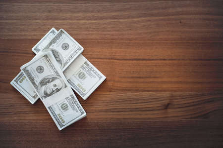 top view of stacking 100 American dollars banknotes on vintage wooden desk using for backgroundの写真素材