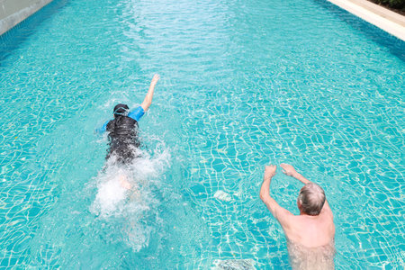 high angle view happy elderly caucasian husband and elderly asian wife swimming in pool during...