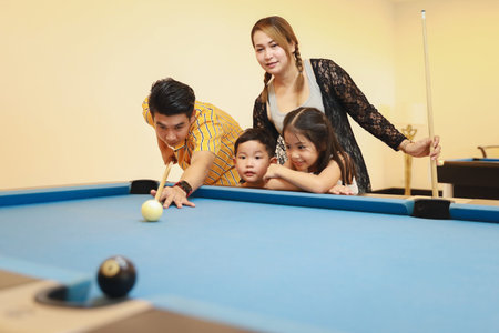 group of happiness asian family father, mother, son and daughter playing billiard or snooker on blue...