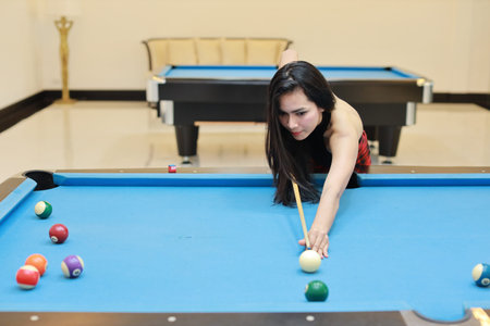 young beautiful asian woman playing and aiming for billiards ball on blue pool table in club