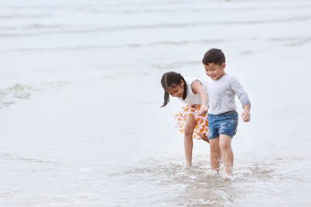happy asian little boy and girl playing and running while holding hand on sandy beach with happy smiling face on sunny dayの写真素材