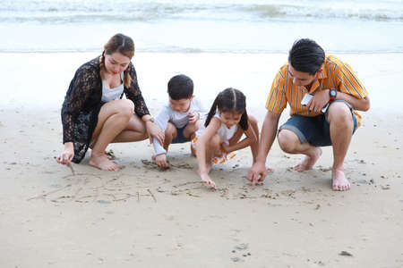 happy asian family father and mother playing with their children boy and girl, they playing and writing something on sandy beach during sunny day with laughing and smilingの写真素材