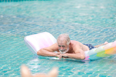 happy elderly caucasian swimming and playing rubber boat in swimming pool during retirement holiday with relaxation and smiling faceの写真素材