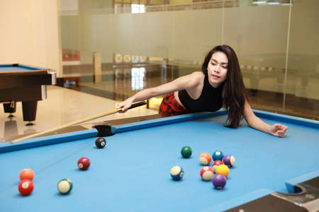 young beautiful asian woman playing and aiming for billiards ball on blue pool table in clubの写真素材