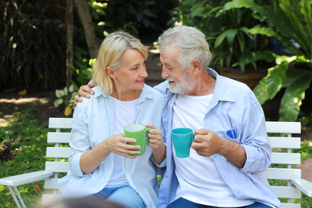 caucasian elderly couple with blue shirt and blue jean sitting and drinking coffee in garden during...