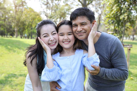 image of happy family, daughter putting her hands on parents cheek with smiling during summer time in the parkの写真素材