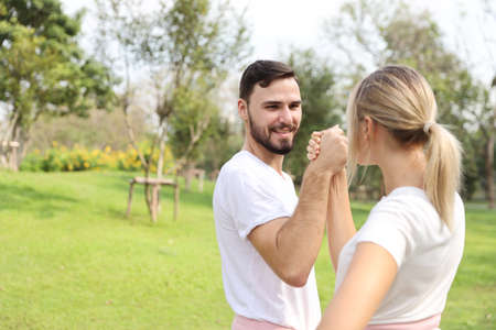 image of young caucasian couple in white and pink sport dress with smiling and arm wrestling challenge in the park with green tree in natureの写真素材