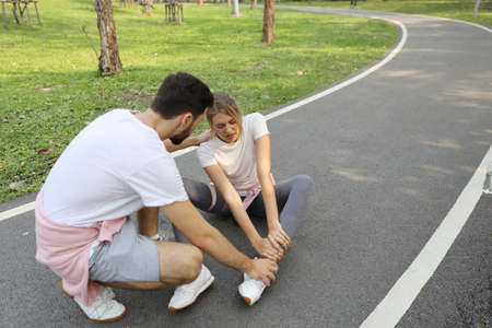 young caucasian girl fall down because of the dizziness from too much exercise and young man is helping in the parkの写真素材