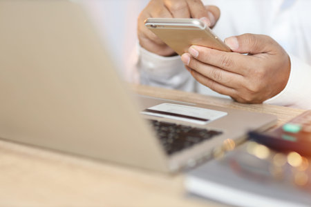 Man hands in white shirt sitting and looking credit card and using laptop computer on table for...