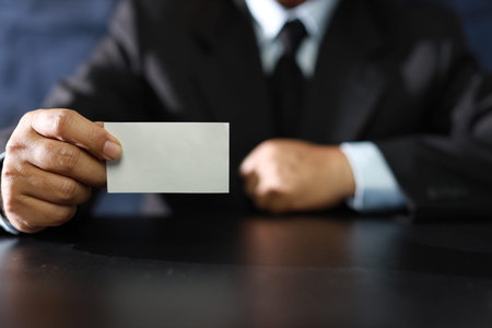 Business man hands in black suit sitting and showing or giving blank business name card while...