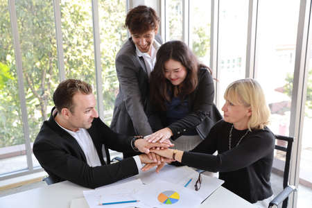 medium shot multiethnic business people sitting in office meeting room and stacking hands together meaning of teamwork concept with happy smiling faceの写真素材