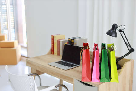 Shopping bags on wooden working table with computer black blank screen and books in room house indoor. Free space for your advertisementの写真素材