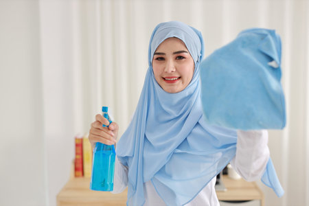 Indoor shot active young beautiful asian muslim housewife woman holding cleaning spray, washing...