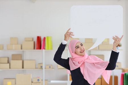 Active asian muslim woman in blue suit standing and holding white speech bubble with online package...