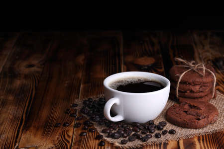 White cup of americano coffee with chocolate chip cookie on dark vintage wooden tableの写真素材