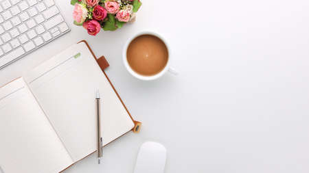 Top view white wooden workspace office desk with computer and office supplies. Flat lay work table with blank notebook, keyboard, flower and coffee cup. Copy space for your advertising content.の写真素材