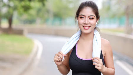 Portrait sporty young asian woman in sportswear jogging outdoor for marathon training. Jogger girl exercising along concrete path outdoor with green tree background. Sport conceptの写真素材