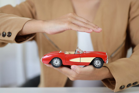 Young active business woman hands in casual dress sitting while holding and protecting car model or automobile on white table. Insurance and security conceptの写真素材