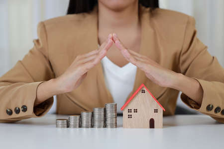 Young active business woman hands in casual dress sitting and protecting house model on white table. Property insurance and security conceptの写真素材