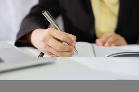 Businesswoman hands in black suit sitting and writing notebook and working or using computer on white table with business chart and calculator in modern office with paper workの写真素材