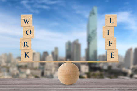Wooden block with words work and life on wooden seesaw balancing on wood desk with city background