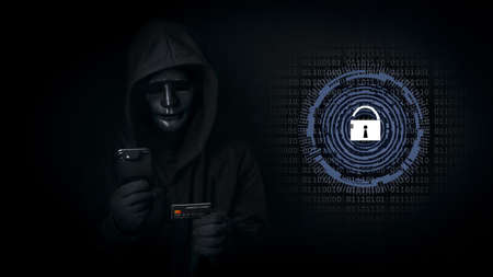 Dangerous anonymous hacker man in hooded and mask use smartphone and credit card, break security data and hack password with key unlocked. Internet crime, cyber attack security conceptの写真素材