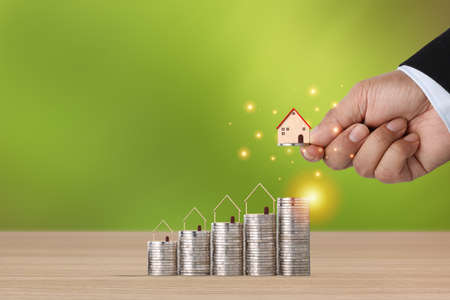 Business property investment with business man hand stacking coin growing growth with house model on wooden desk with green background for financial real estate advertising conceptの写真素材