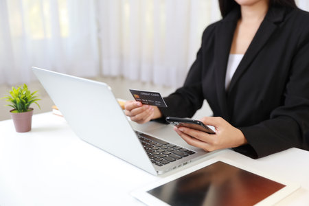 Woman hands sitting and holding smartphone and using computer  and tablet with credit card for online payment or shopping online. Business woman using internet while working. E-Banking conceptの写真素材