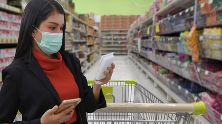 Young smart business asian woman shopper with face mask choosing grocery to buy from shelf in...