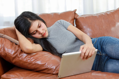 Young smart and active asian female lying on sofa in living room, using tablet with happy smiling face, Lifestyle and technologyの写真素材