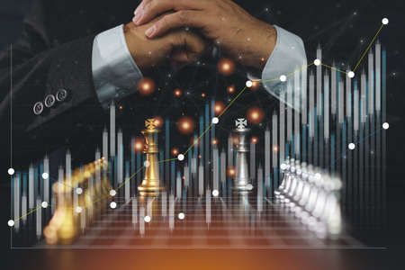 Businessman hands control chess board game of business strategy and tactic with futuristic graphic icon and chart stock trading. Idea for management competition, success and leadership.の写真素材